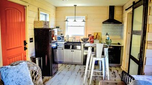 A compact kitchen with wooden walls, a refrigerator, a microwave, a sink, and a window.