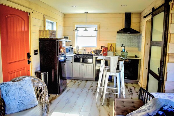 A compact kitchen with wooden walls, a refrigerator, a microwave, a sink, and a window.