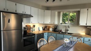 A modern kitchen with white cabinets, stainless steel appliances, a wooden dining table, and a window providing natural light. - Lake Whatcom Summer home, 100' private beach, paddle boards and kayaks! (Bellingham)