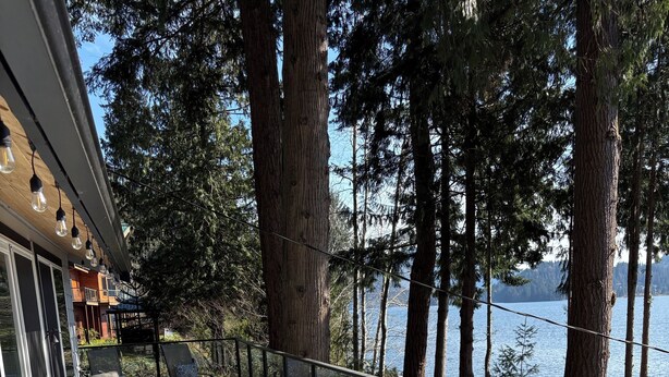 An outdoor seating area with chairs and a table, overlooking a lake and surrounded by trees. - Lake Whatcom Summer home, 100' private beach, paddle boards and kayaks! (Bellingham)