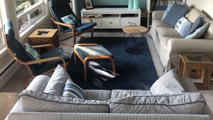 A living room with a sofa, chairs, a TV, and a bookshelf. - Lake Whatcom Summer home, 100' private beach, paddle boards and kayaks! (Bellingham)