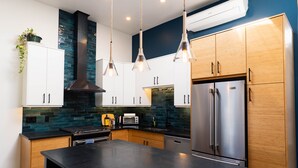 Een moderne keuken met houten kastjes, een zwart aanrecht, roestvrijstalen apparatuur en hanglampen.