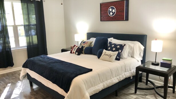A neatly arranged bedroom with a large bed, a nightstand, a ceiling fan, and a wall-mounted lamp. - Cumberland Cottage, 1 level house just off I-24, near Murfreesboro and Nashville (Murfreesboro)