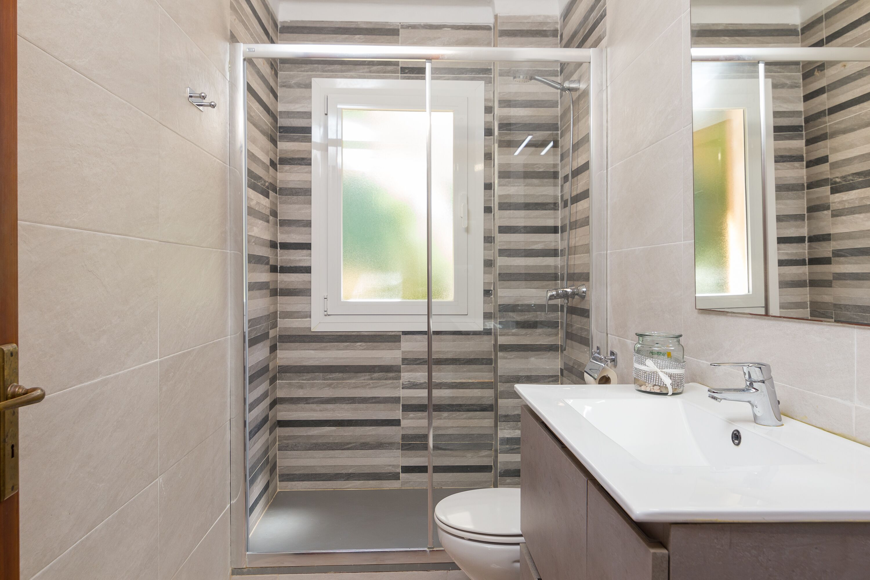 A modern bathroom with a glass-enclosed shower, a white sink, and a large mirror.