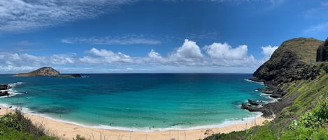 A coastal landscape with a sandy beach, clear turquoise waters, and rocky cliffs.
