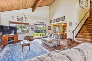 Relax in a spacious living area with a high ceiling, featuring a large flat-screen TV, comfortable sofa, and a small table.