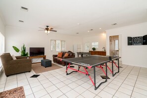 Un salon équipé d’une table de ping-pong, d’un canapé, d’un téléviseur et d’un ventilateur de plafond.