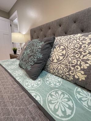 A bedroom with a tufted headboard, a patterned bedspread, and decorative pillows. - Beautiful & Cozy 2bd/1b Near O’Hare & Metra (MD-W) (Elmwood Park)