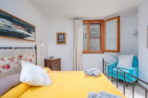 A room with a bed, a chair, a window, and a painting on the wall.