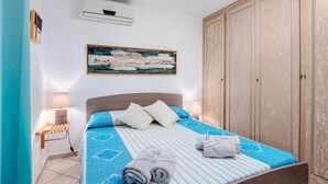 A neatly made bed with a patterned bedspread, a headboard, a wall-mounted air conditioner, a painting, and a wardrobe. - Panoramic Holiday Apartment "Isuledda" with Sea View, Shared Pool & Air Conditioning (San Teodoro)