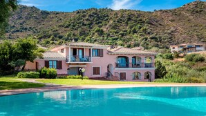 A two-story house with a swimming pool, surrounded by greenery and hills. - Panoramic Holiday Apartment "Isuledda" with Sea View, Shared Pool & Air Conditioning (San Teodoro)
