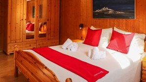 Un dormitorio de madera con una cama, almohadas rojas y blancas, una manta roja y un cuadro en la pared.