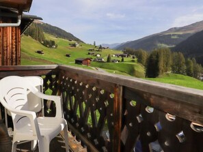 Un balcon doté d’une balustrade en bois, donnant sur une vallée verdoyante parsemée de maisons.