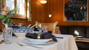 Una mesa de comedor dispuesta con un bol, vasos y cubiertos, con un jarrón de flores y un cuadro en la pared.