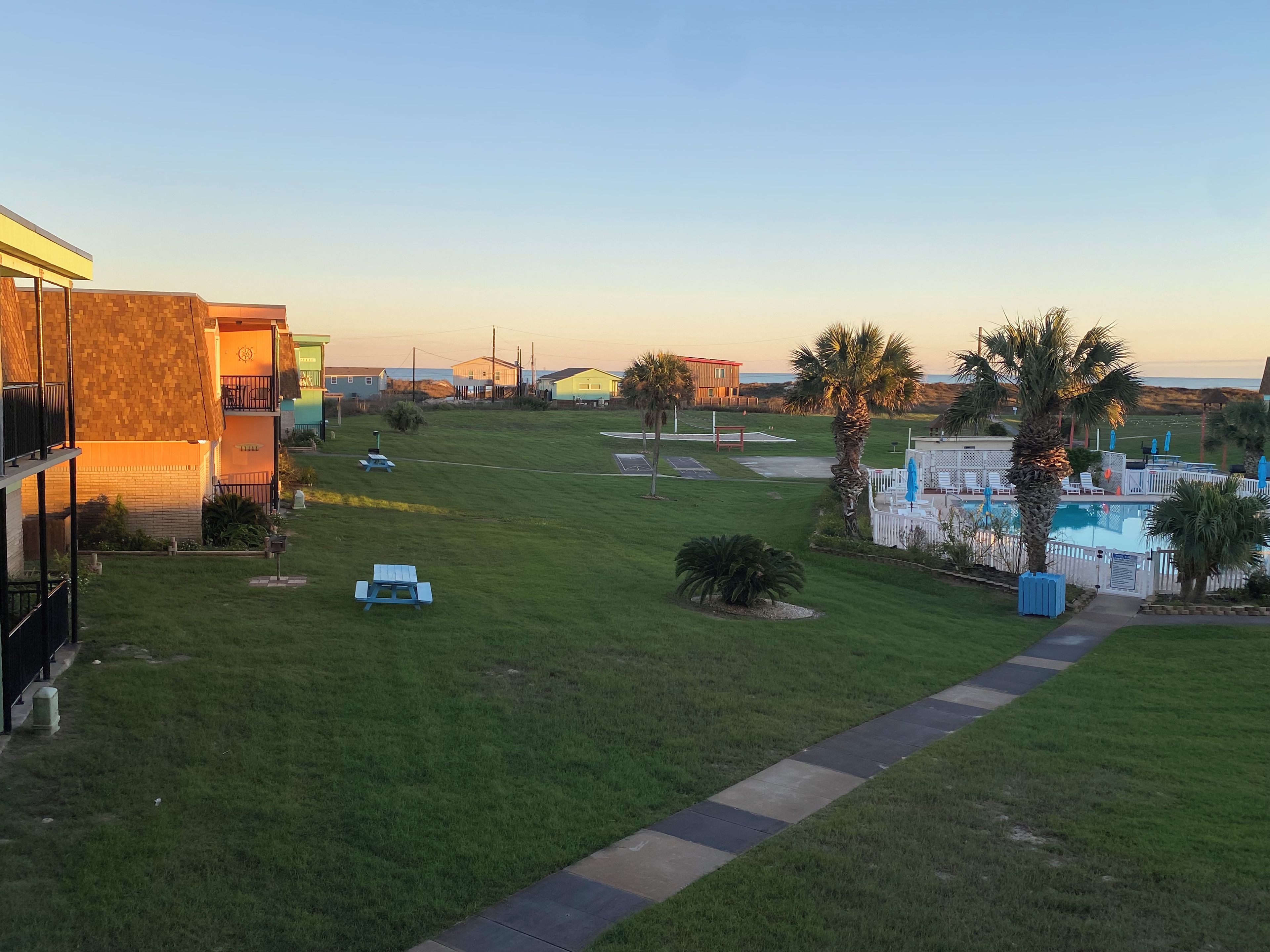 A grassy area with a pool, palm trees, and a building with a balcony.