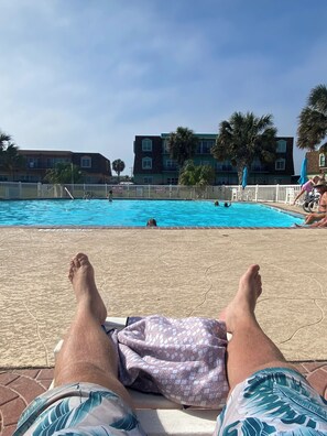 Blick über den Pool bei blauem Himmel, mit Gebäuden im Hintergrund.