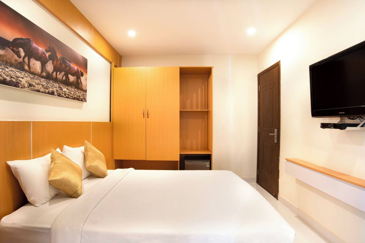 A hotel room with a large bed, wooden wardrobe, a television, and a painting on the wall.