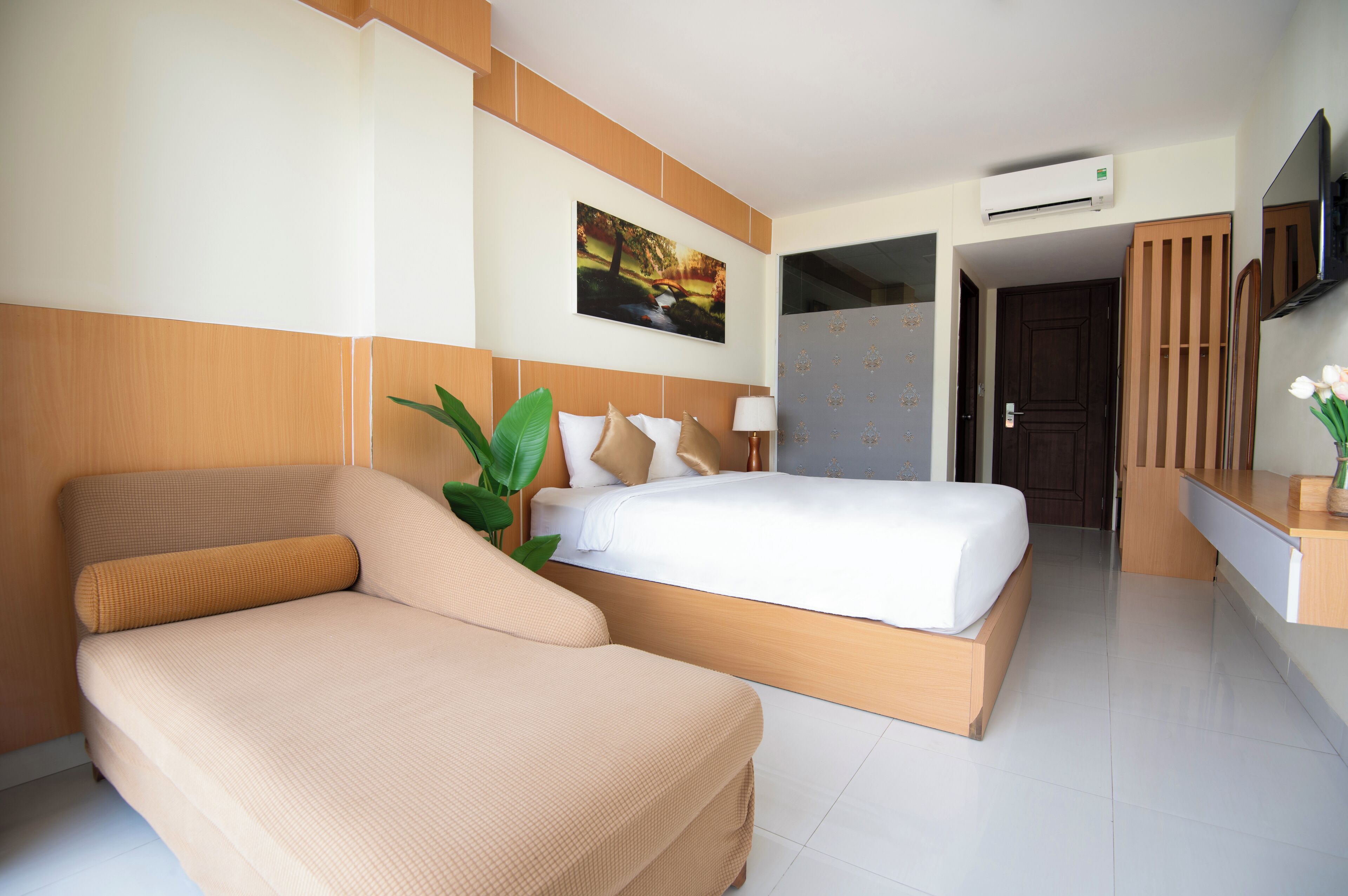 A modern hotel room with a large bed, a sofa, a desk, and a TV.