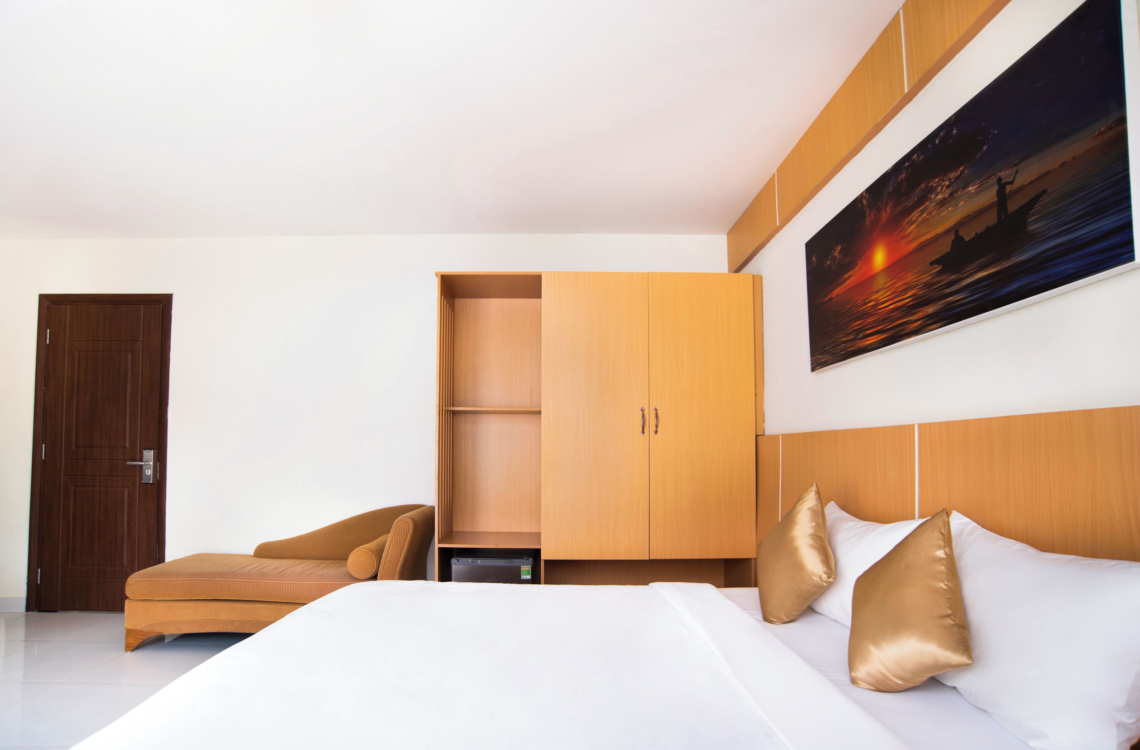 Una habitación de hotel moderna con una cama, un armario de madera, un escritorio y un cuadro de un atardecer.