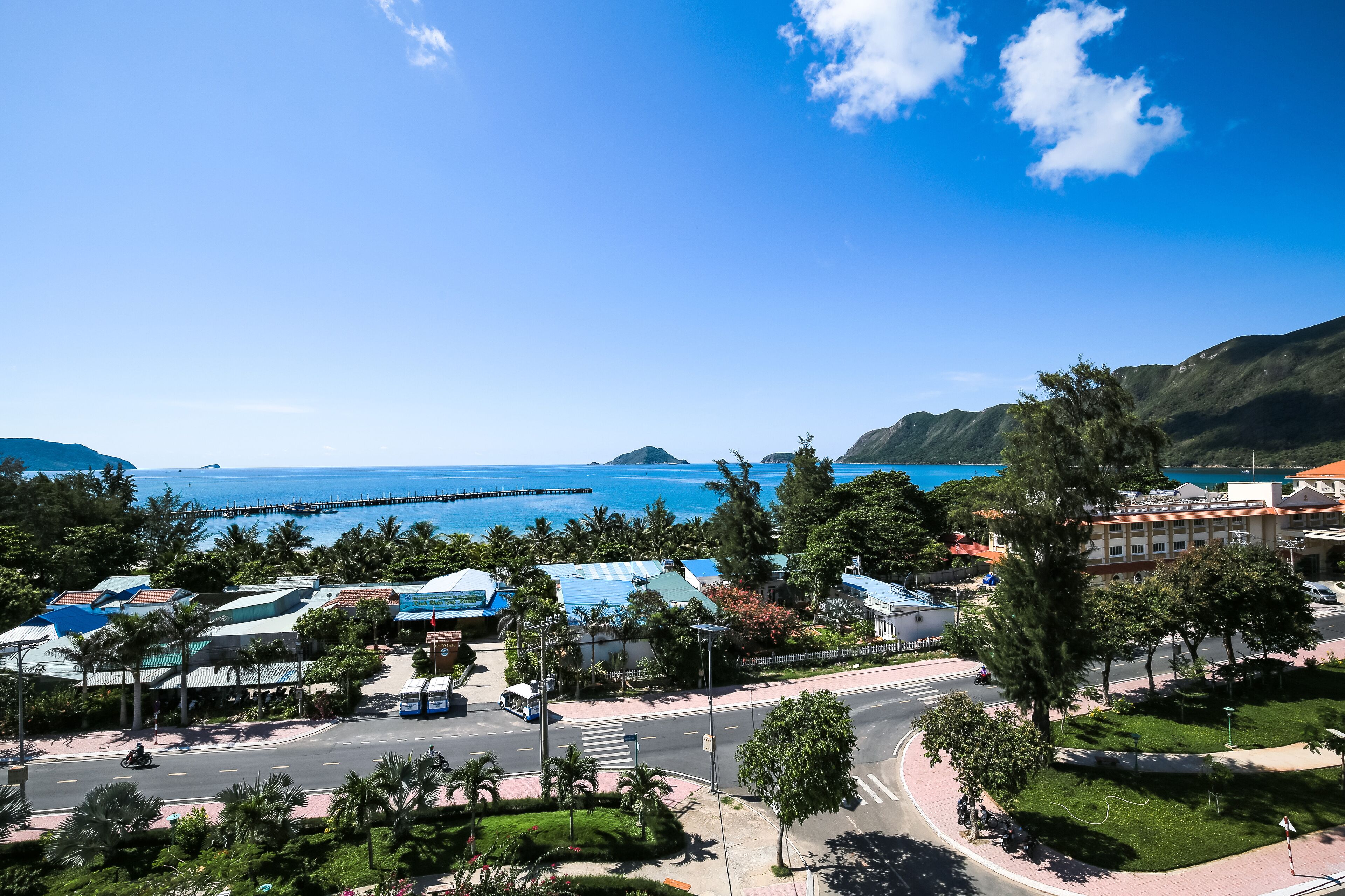 A coastal town with a clear view of the sea, a road with vehicles, and buildings with blue roofs.