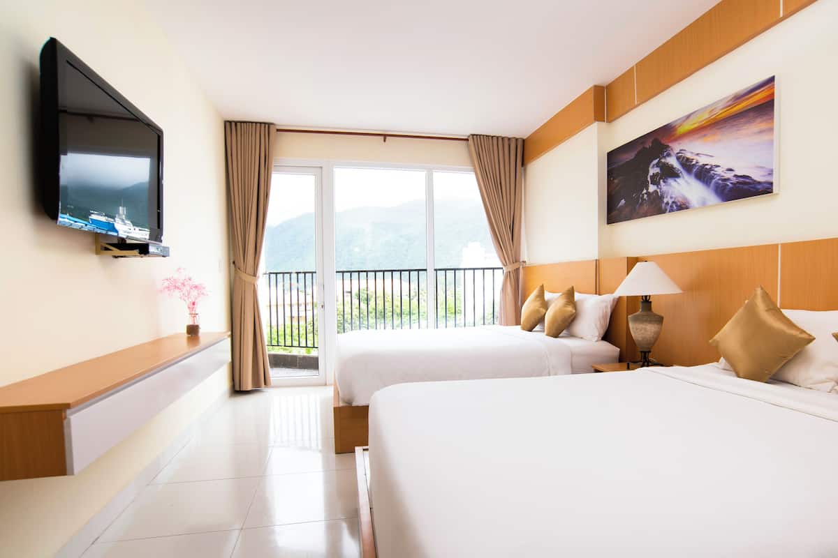 A hotel room with two beds, a TV, a painting, and a balcony with a view of mountains.