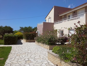 A two-story house with a stone pathway leading to the entrance, surrounded by well-maintained gardens and a clear blue sky.