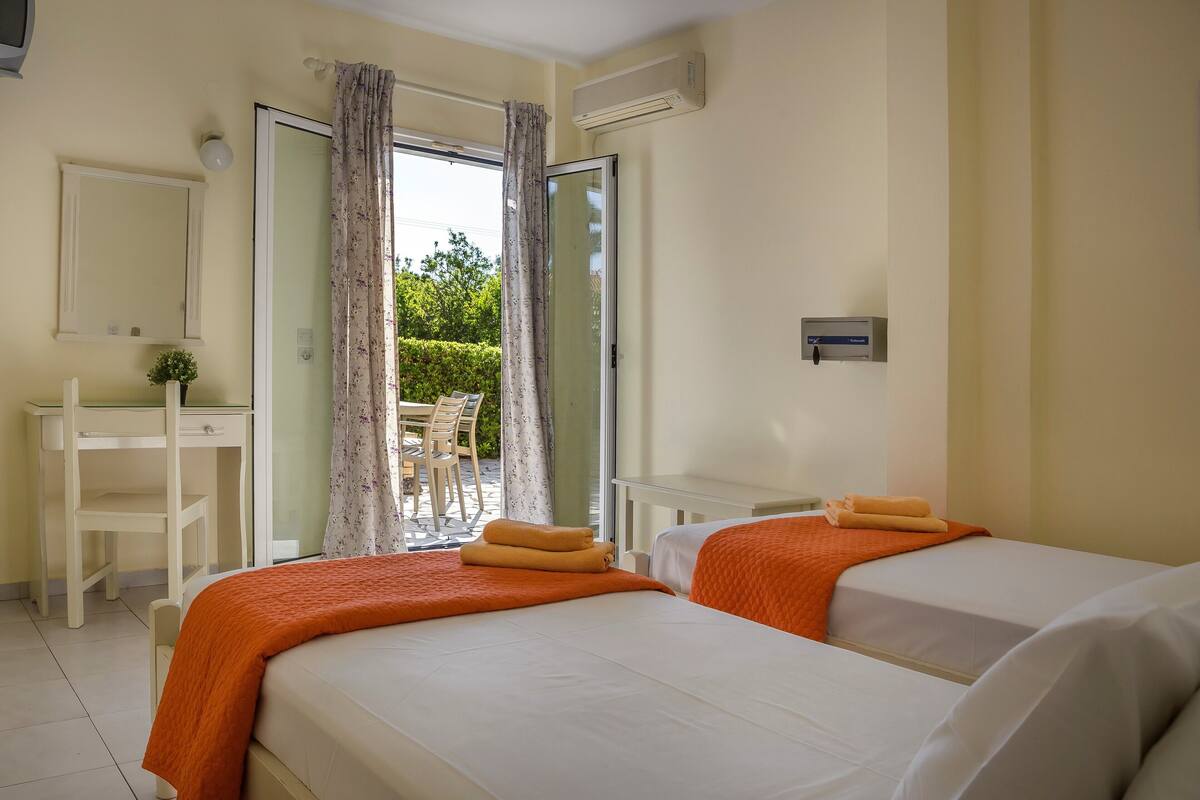 Ein Hotelzimmer mit zwei Betten, einem Schreibtisch, einem Stuhl und einer Schiebetür zum Außenbereich.