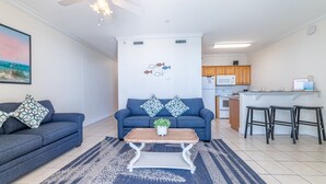 A living room with a blue sofa, a wooden coffee table, and a kitchen in the background.