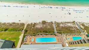 An aerial view of a beach resort with a swimming pool, beach umbrellas, and lounge chairs.