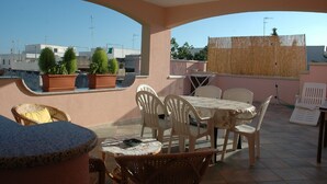 A covered outdoor patio with a table and chairs, potted plants, and a view of the surrounding buildings. - Vacation House in S. Maria di Leuca 900m from the sea (CASTRIGNANO DEL CAPO)
