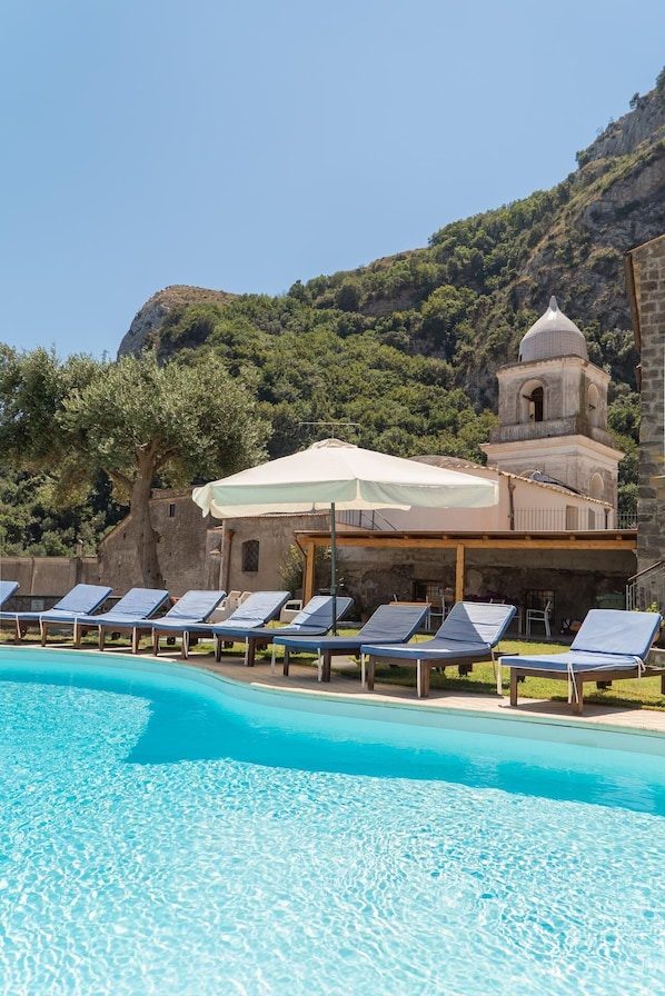 Un área de piscina con sillones, una zona de estar cubierta y un edificio con un campanario.