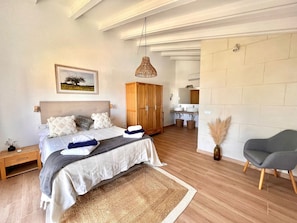 Een slaapkamer met een bed, nachtkastje, houten garderobe, badkamer met wastafel en spiegel, en een stoel.