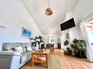 Een ruime woonkamer met een grijze bank, een houten salontafel en grote ramen.