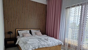 A bedroom with a wooden bed frame, a nightstand, a lamp, and a window with lace curtains. - Apartment "Küstenperle"; top floor apartment with large terrace (Świnoujście)