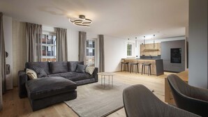 A modern living room with a sectional sofa, a round coffee table, and a kitchen area in the background. - R6 Tegernsee - Apartment TOP 5 upstairs (Bad Wiessee)