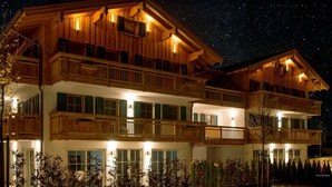 A multi-story wooden building with balconies and large windows, illuminated at night. - R6 Tegernsee - Apartment TOP 5 upstairs (Bad Wiessee)