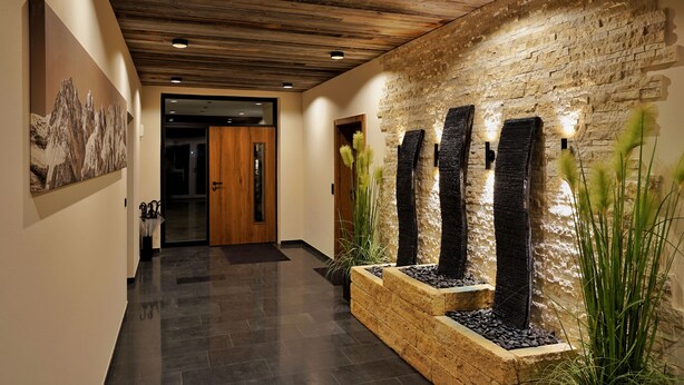 A hallway with a wooden ceiling, a stone wall, and a water feature with vertical elements. - R6 Tegernsee - Apartment TOP 5 upstairs (Bad Wiessee)