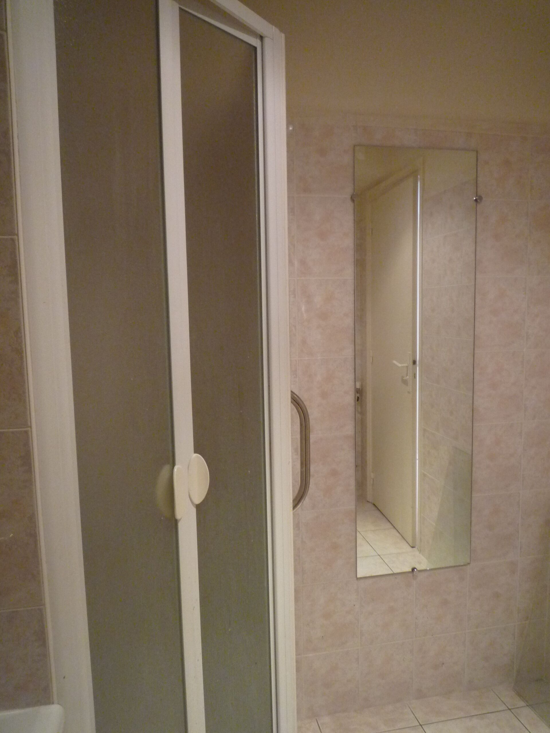 A bathroom with a glass shower door, a mirror on the wall, and beige tiles.