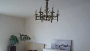 A dining area with a wooden table, four chairs, a chandelier, a radiator, a plant, and a piece of wall art. - Large bright apartment with garage Centre Quimper (Quimper)
