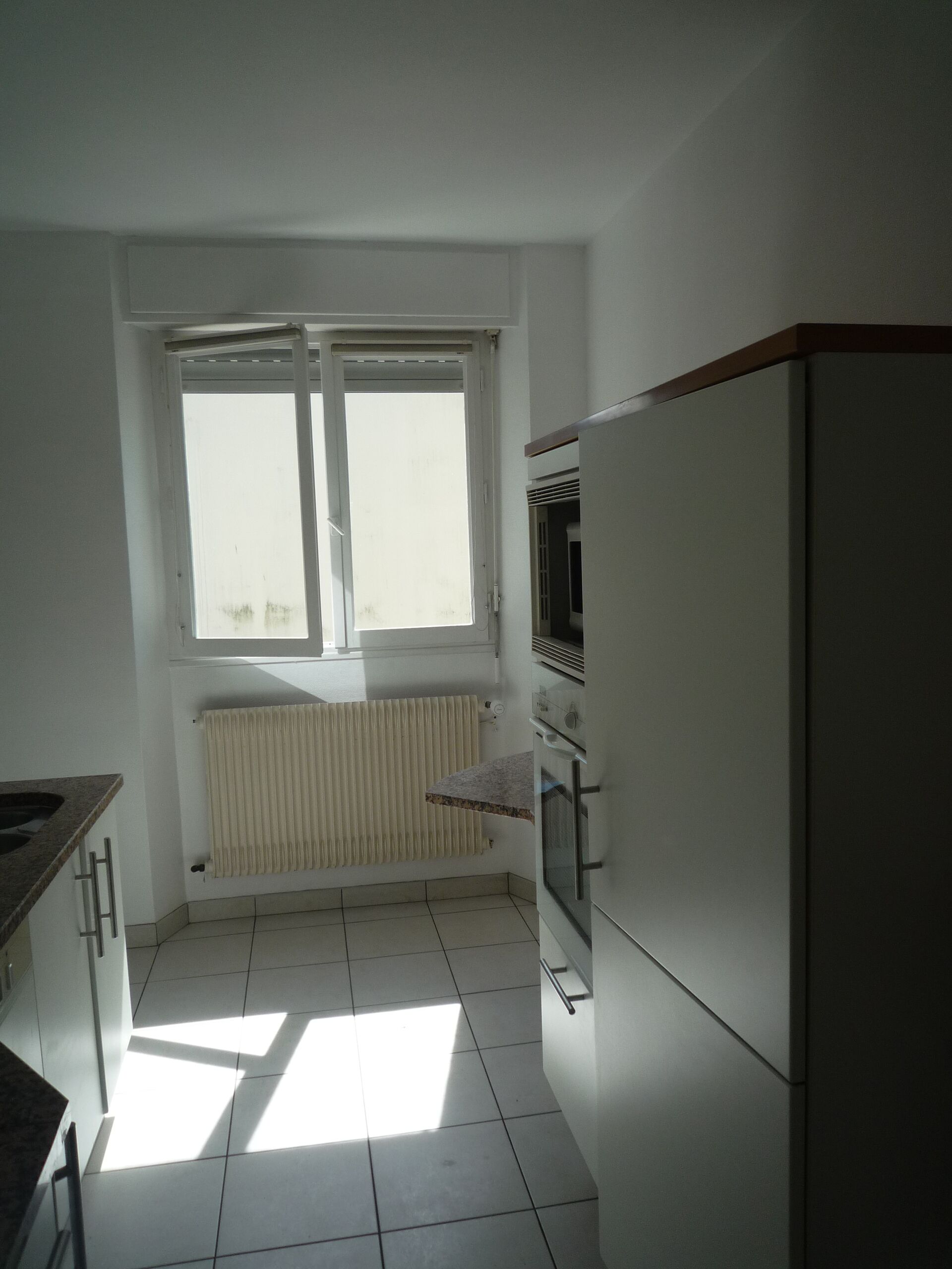 A kitchen with a window, a radiator, and a refrigerator.