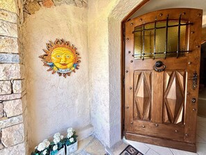 A wooden door with a metal grid, a decorative sun with a face, and a stone wall with a stone staircase.