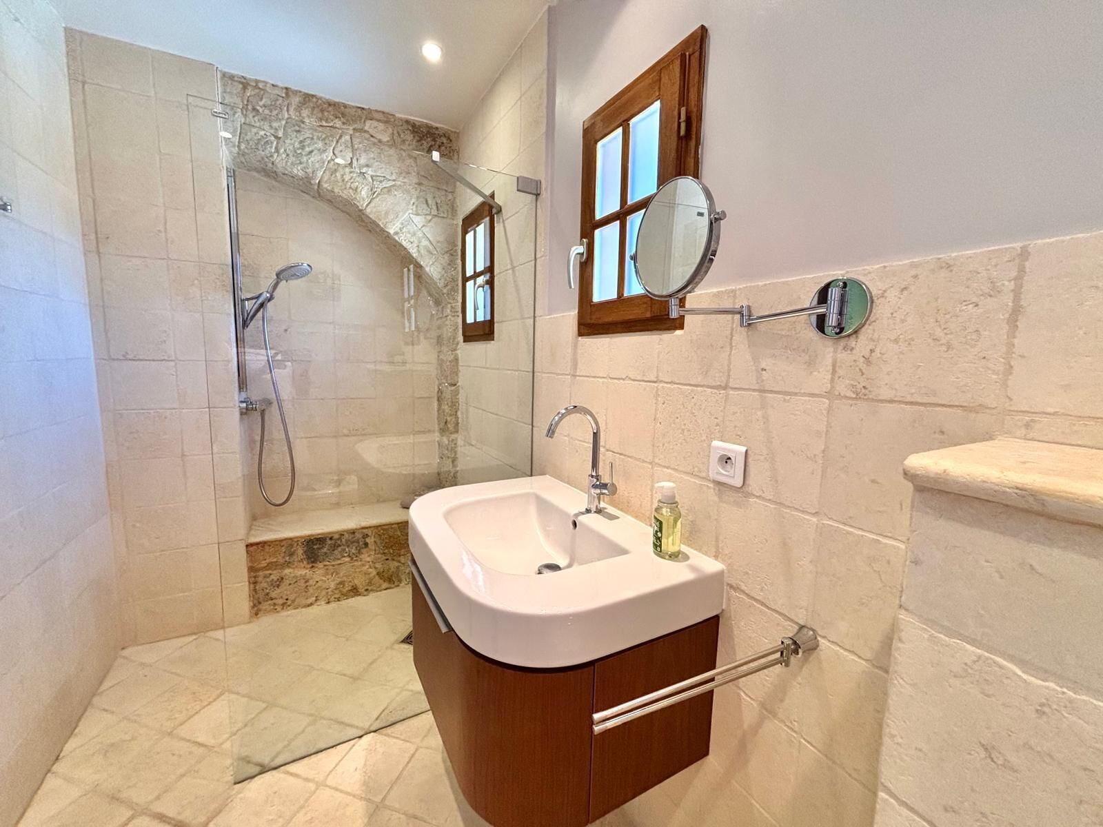Un baño con ducha, lavamanos, espejo y ventana.