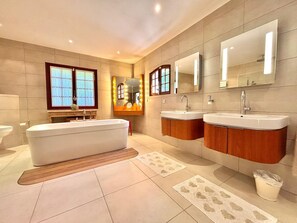 A modern bathroom with a freestanding bathtub, two vanity sinks, and large mirrors.