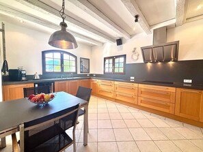 A modern kitchen with wooden cabinets, a black countertop, a dining table with chairs, and a hanging pendant light.