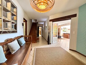 A spacious hallway with a wooden bench, a staircase, and a large open door leading to another room.