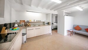 Une cuisine moderne avec des meubles blancs, un four encastré et un four à micro-ondes. On y trouve également un coin repas avec un canapé gris et une petite table.