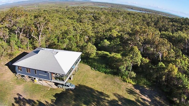 Une maison dotée d’une grande terrasse, entourée d’une forêt dense et offrant une vue sur une étendue d’eau lointaine.