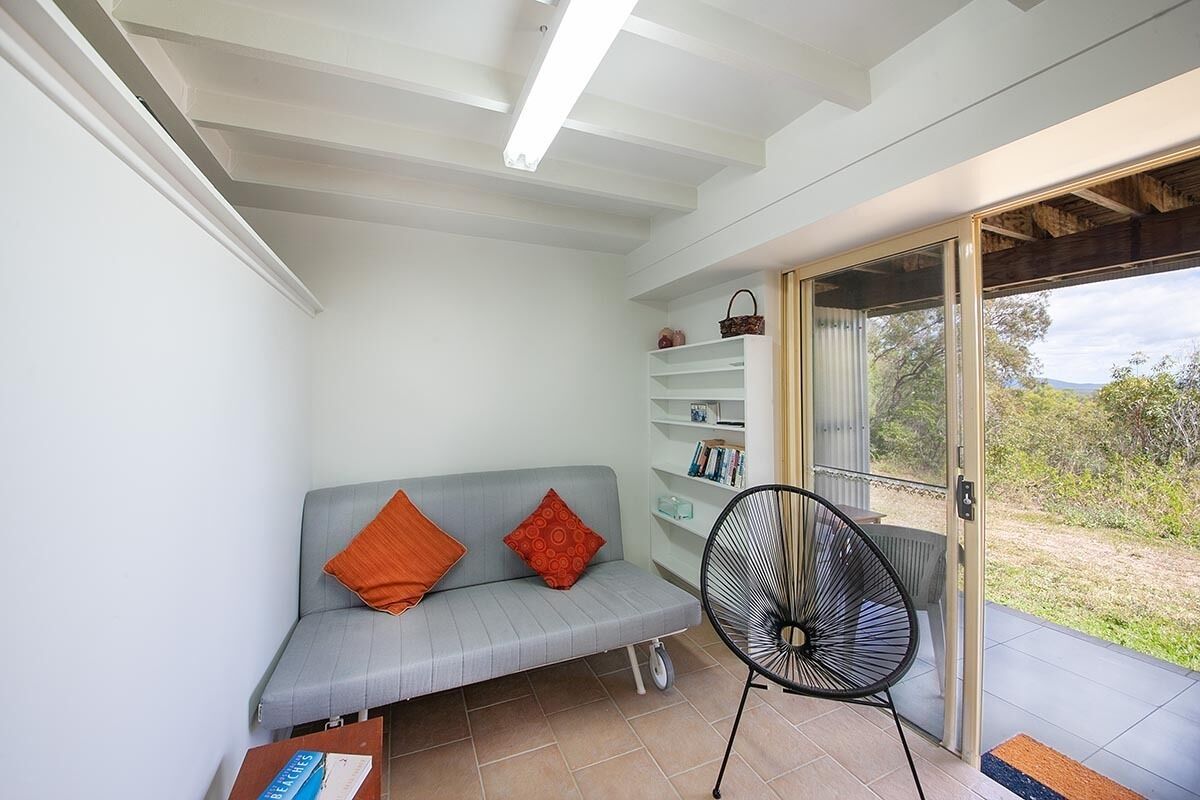 A room with a grey sofa, a black fan, and a glass door leading outside.