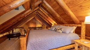 Un dormitorio acogedor en el ático con techo de madera, una cama con colcha acolchada y un pequeño banco de madera.