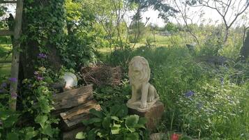 Una estatua de jardín de un león sobre un pedestal de piedra, rodeada de exuberante follaje y flores.